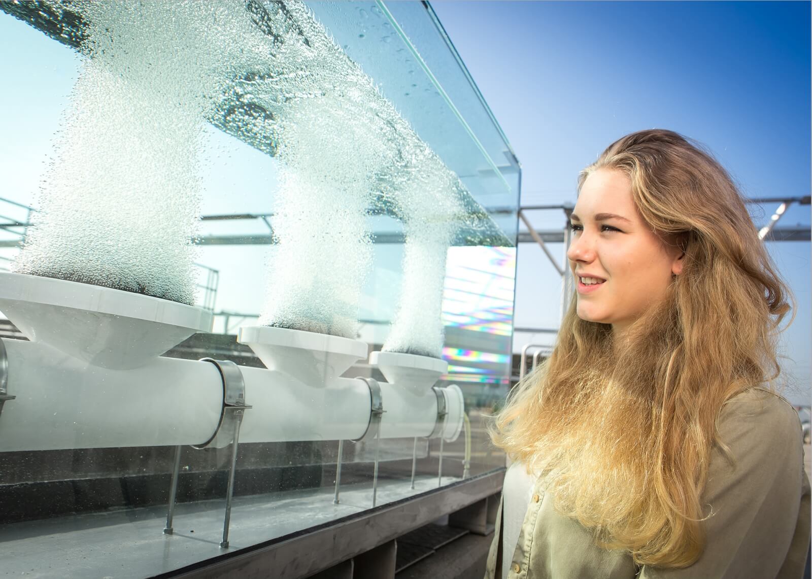 Das Bild zeigt eine junge Frau, die auf drei luftsprudelnde Tellerbelüfter in einem Plexiglas-Kubus blickt.